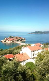 High angle view of houses by sea against clear blue sky