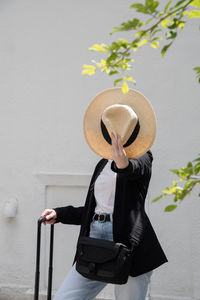 Rear view of woman wearing hat standing against wall
