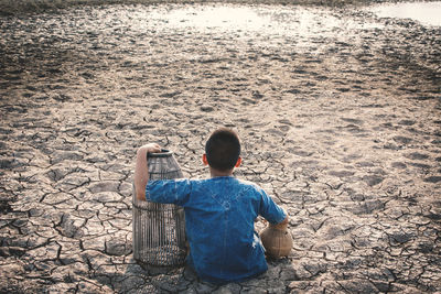 High angle view of boy sitting on field during drought