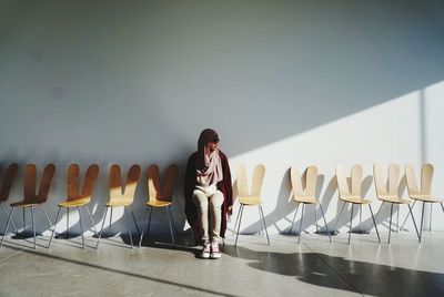 Woman sitting on chair against wall