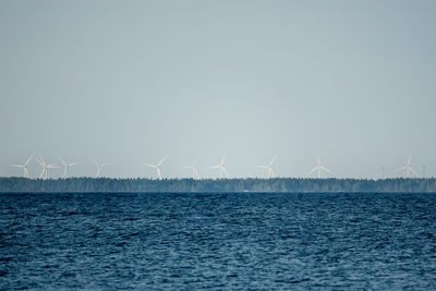 Wind turbines by sea against sky