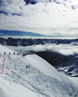 People on snowcapped mountains against cloudy sky