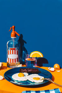 Studio shot of bottle of soda, glass of soda with slice of lemon and plate of fried eggs with chorizo