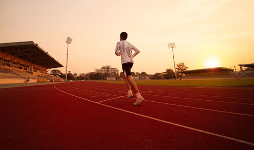 Full length of teenage boy running on sports track against orange sky