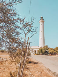 Lighthouse amidst trees and buildings against sky