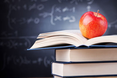 Close-up of apple on stacked books against blackboard