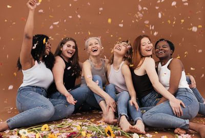 Group of happy women sitting on the brown background while petals from flowers falling