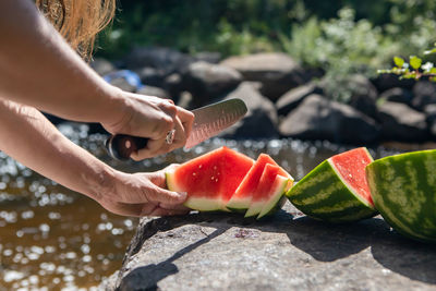 Cropped hand of woman cutting watermelon by lake