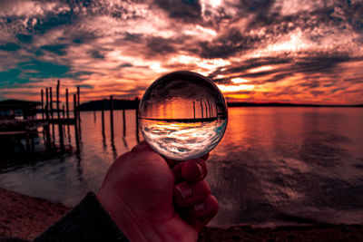 Person holding glass against sea during sunset