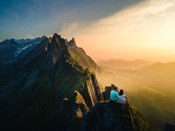 People on rock against sky during sunset