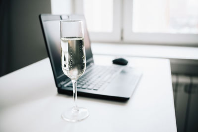 Laptop and glass of champagne on white table at home kitchen, work from home