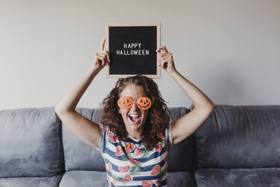 Portrait of woman in novelty glasses holding happy halloween text at home