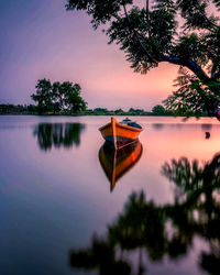 Boat moored on lake against sky during sunset
