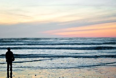 Man standing on beach against sky during sunset