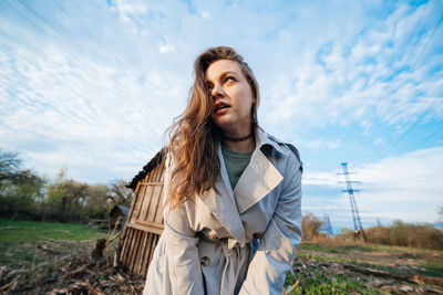 Beautiful girl with long hair in a grey trench coat blue sky background outdoors in spring