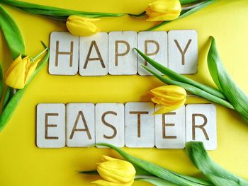 Directly above shot of happy easter text with yellow tulips on table