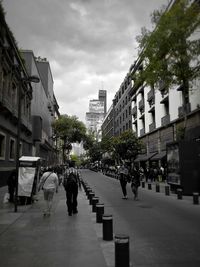 People walking on street amidst buildings in city against sky