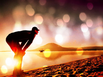 Silhouette man in sea against sky during sunset