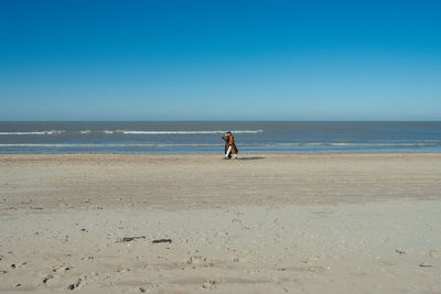 Rear view of woman walking at beach against clear blue sky