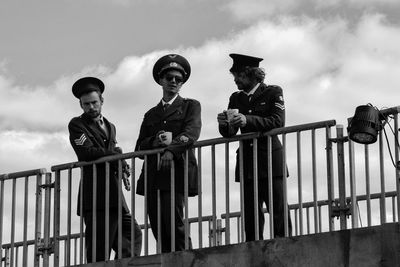 Low angle view of boys on railing against sky