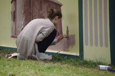 Side view of woman holding camera while standing by grass