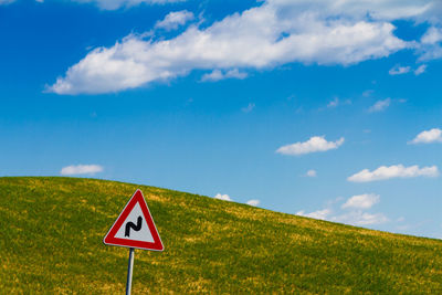 Road sign on field against sky