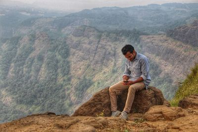 Man sitting on rock against mountains