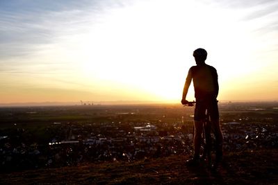 Rear view of silhouette man with bicycle standing on landscape against sky