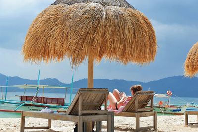 Woman sitting on chair at beach against sky