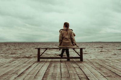 Rear view of woman looking at sea while sitting on bench