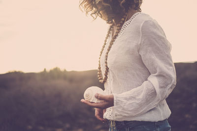 Midsection of woman holding seashell against sky