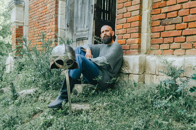 Rest of viking warrior near old brick castle and trees. sword and helmet. pensive look.