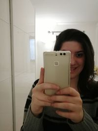 Close-up portrait of smiling young woman using phone at home