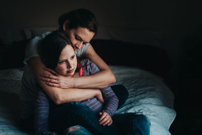 Thoughtful mother and daughter sitting on bed at home