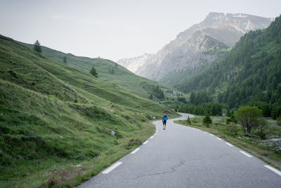 Rear view of man walking by mountain on road