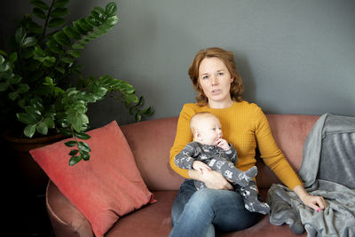 Serious grandmother holding baby grandson on sofa at home living room