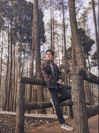 Portrait of young man sitting on tree trunk in forest