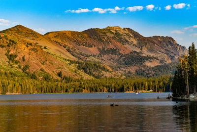 Rusty gold mountain range with iron rich rocks overlooking alpine lake on a blue sky day 