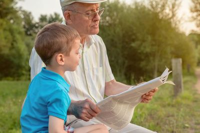 Grandfather reading newspaper while sitting by grandson in park