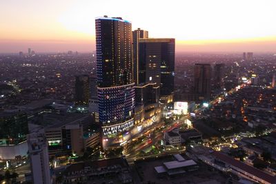 Illuminated buildings in city against sky at sunset