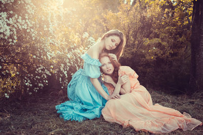 Portrait of young women embracing while sitting by plants outdoors