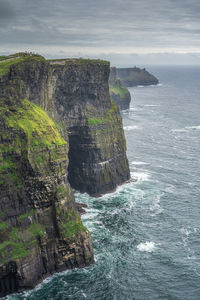 Tourists walking on cliffs of moher with watchtower moher tower on far distance, ireland