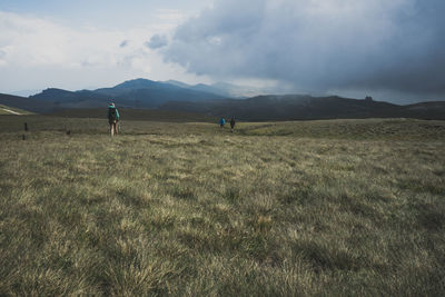 Hikers walking on grassy field against mountains