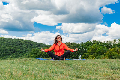 Full length of woman exercising on field against sky