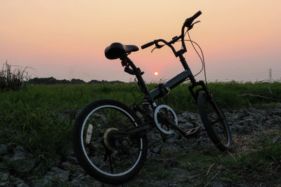 Bicycle parked on field during sunset