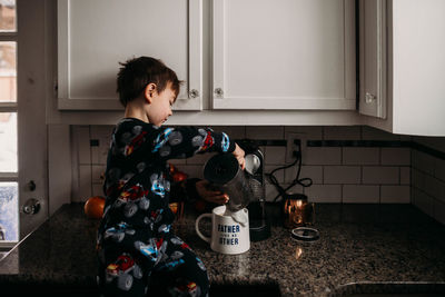 Young boy in kitchen pouring milk into coffee cup for dad