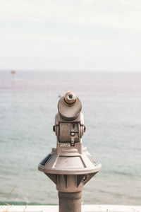 Close-up of coin-operated binoculars on sea against sky