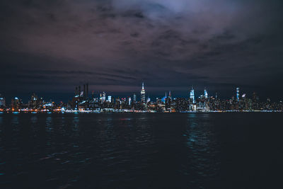 Illuminated city by sea against sky at night