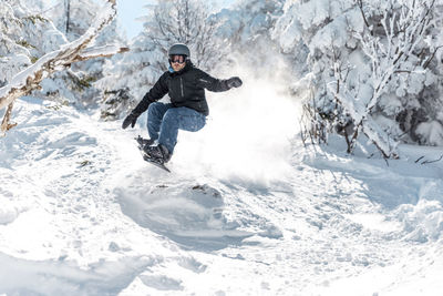 Full length of man snowboarding on snow against trees during winter