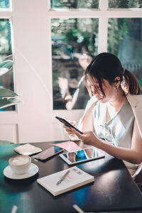 Young woman using mobile phone while sitting on table